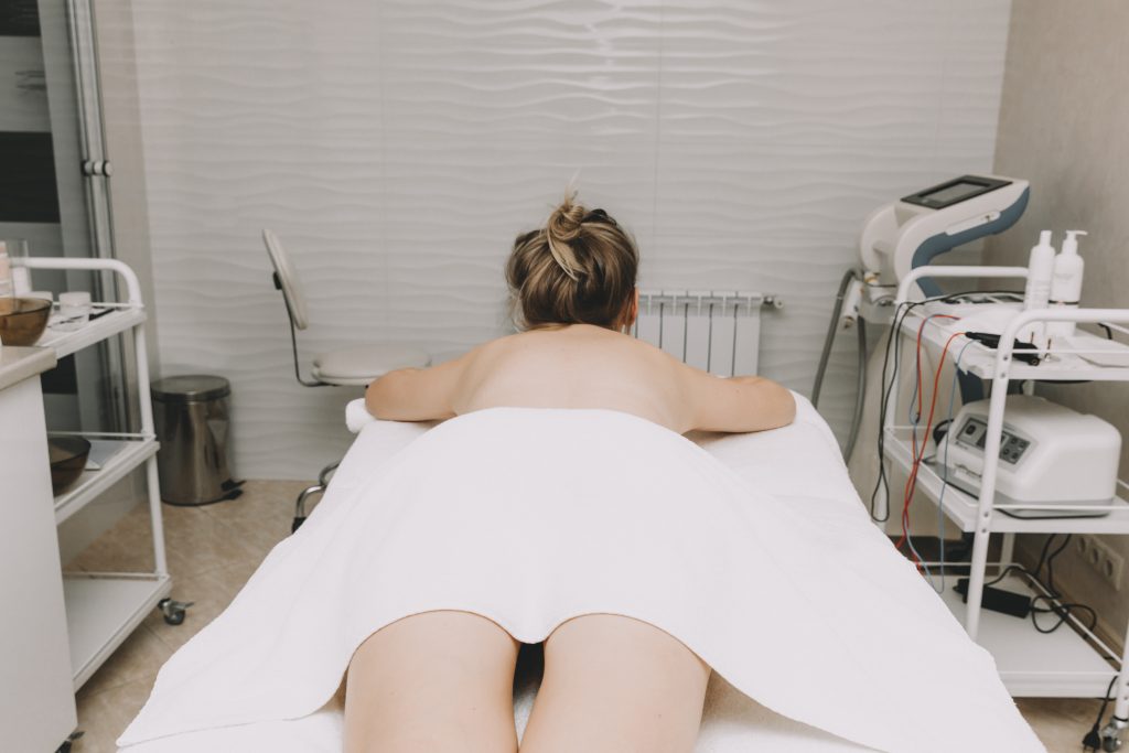 woman doing back massage with bamboo stick in wellness spa center